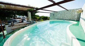 Een zwembad met een stenen muur en een pergola.