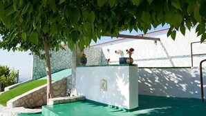 A pool area with a stone wall, a small waterfall feature, and a bench with flowers. - Camagna Country House (Partanna)