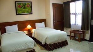 Une chambre d’hôtel avec deux lits, une table de chevet avec une lampe, une table en bois et une porte.