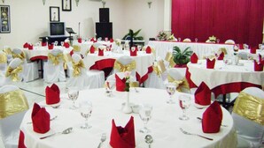 Une salle de banquet avec des tables rondes dressées pour le repas, des nappes blanches et des rubans rouges et dorés.