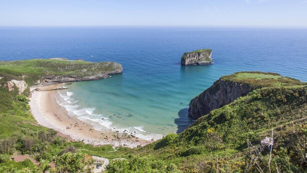 Paisaje costero con una playa, acantilados y una vista despejada del océano.