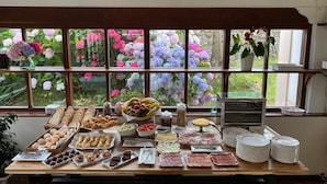 Un bufé de desayuno con diversos pasteles, frutas y embutidos, con vistas a un jardín a través de amplias ventanas.
