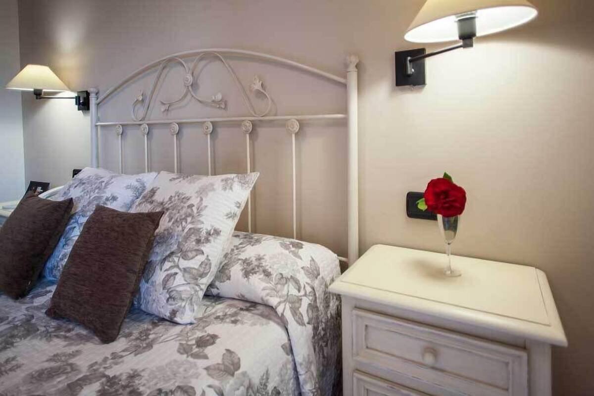 Una cama bien hecha con ropa de cama floral, cabecera blanca y lámparas de noche.