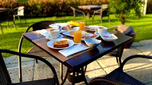 Mesa de desayuno al aire libre con platos de comida, tazas y un vaso de jugo de naranja.