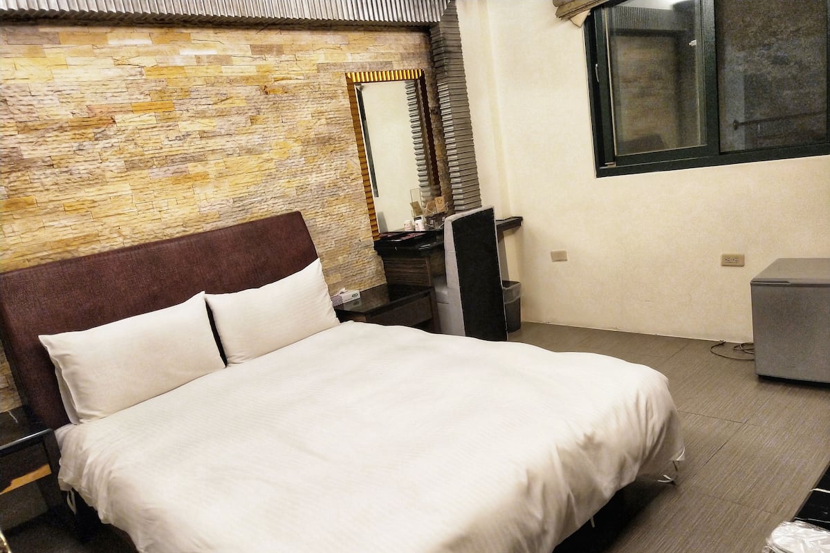 A neatly made bed in a hotel room with a stone wall and a window.