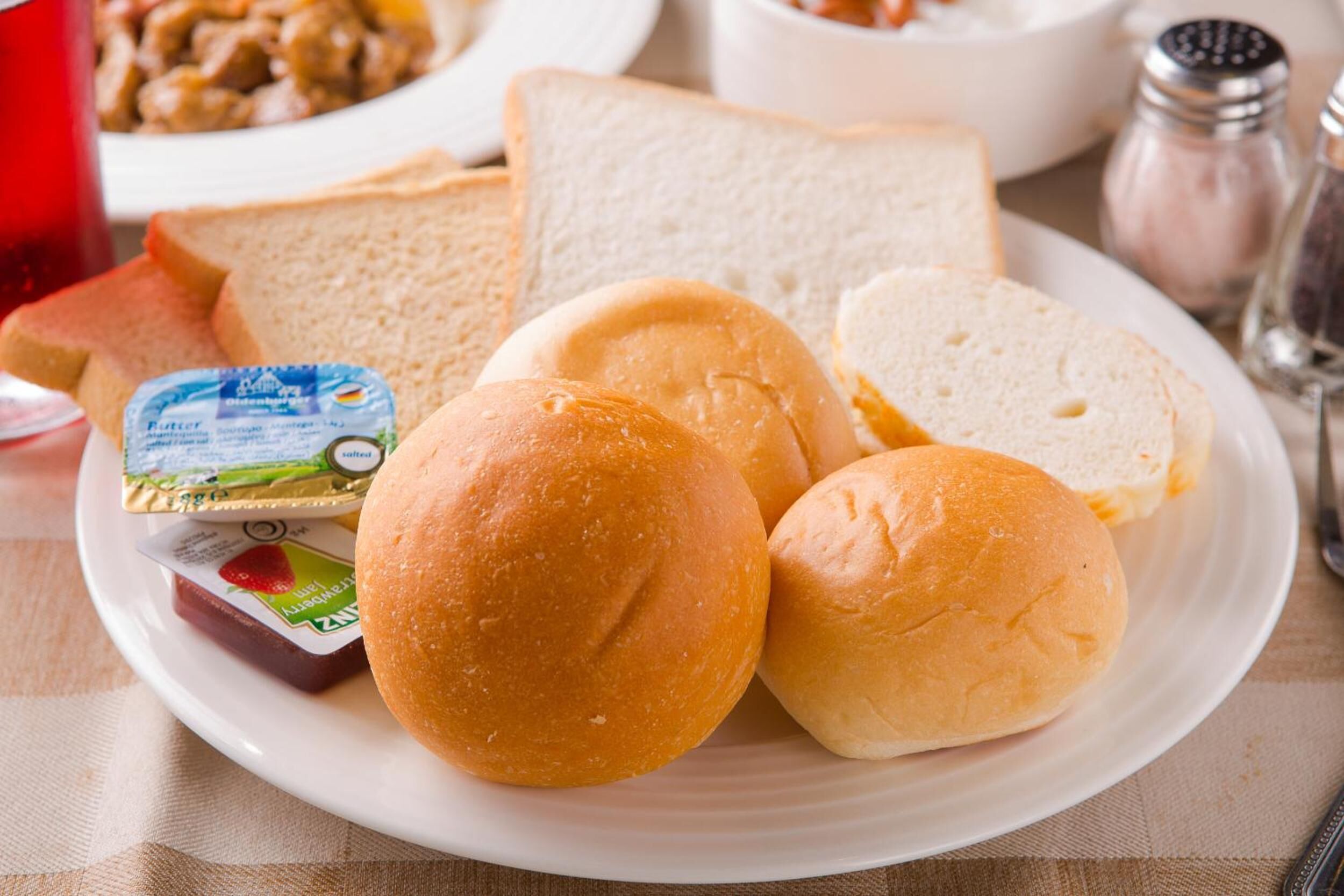 A plate with bread rolls, butter, and jam.