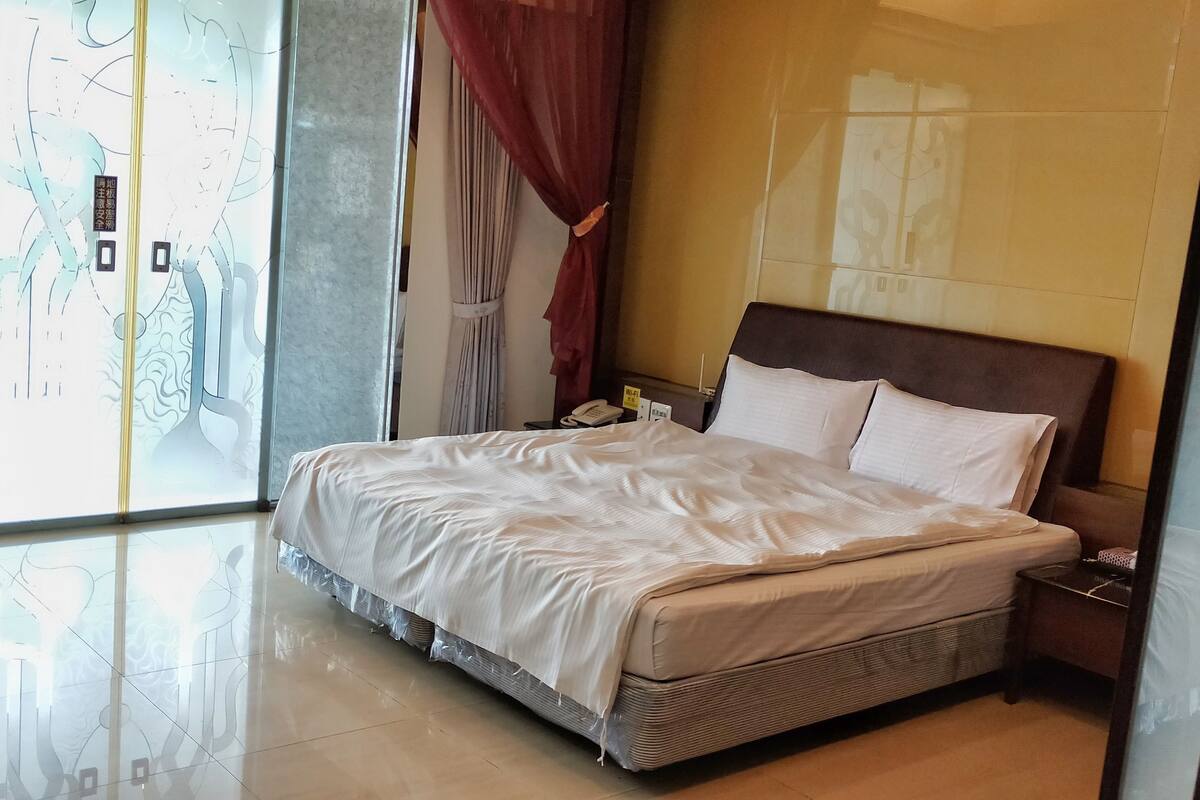 A hotel room with a bed, a bedside table, a phone, and a curtain.