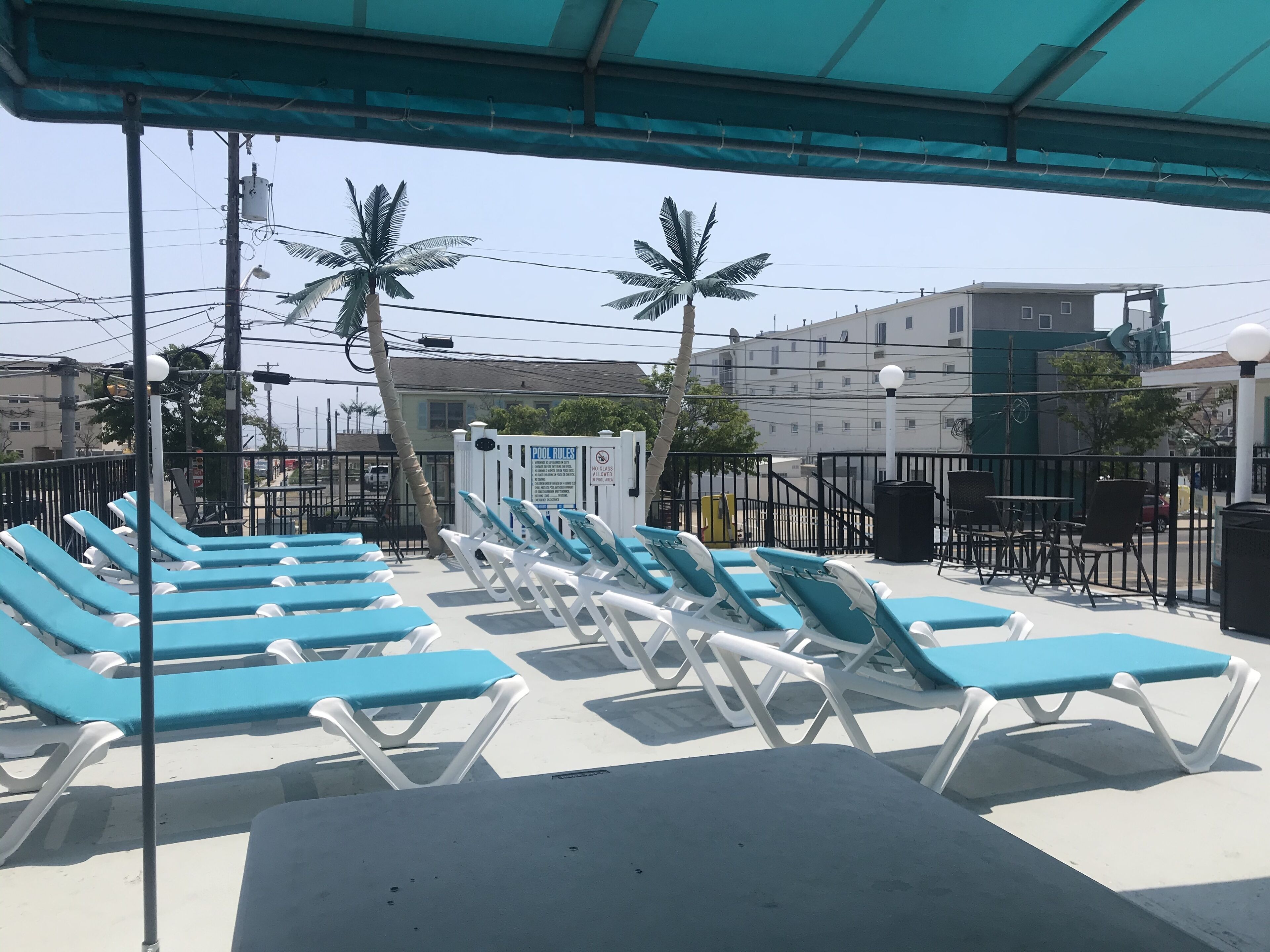 A poolside area with blue and white lounge chairs, a covered seating area, and a sign indicating pool rules.