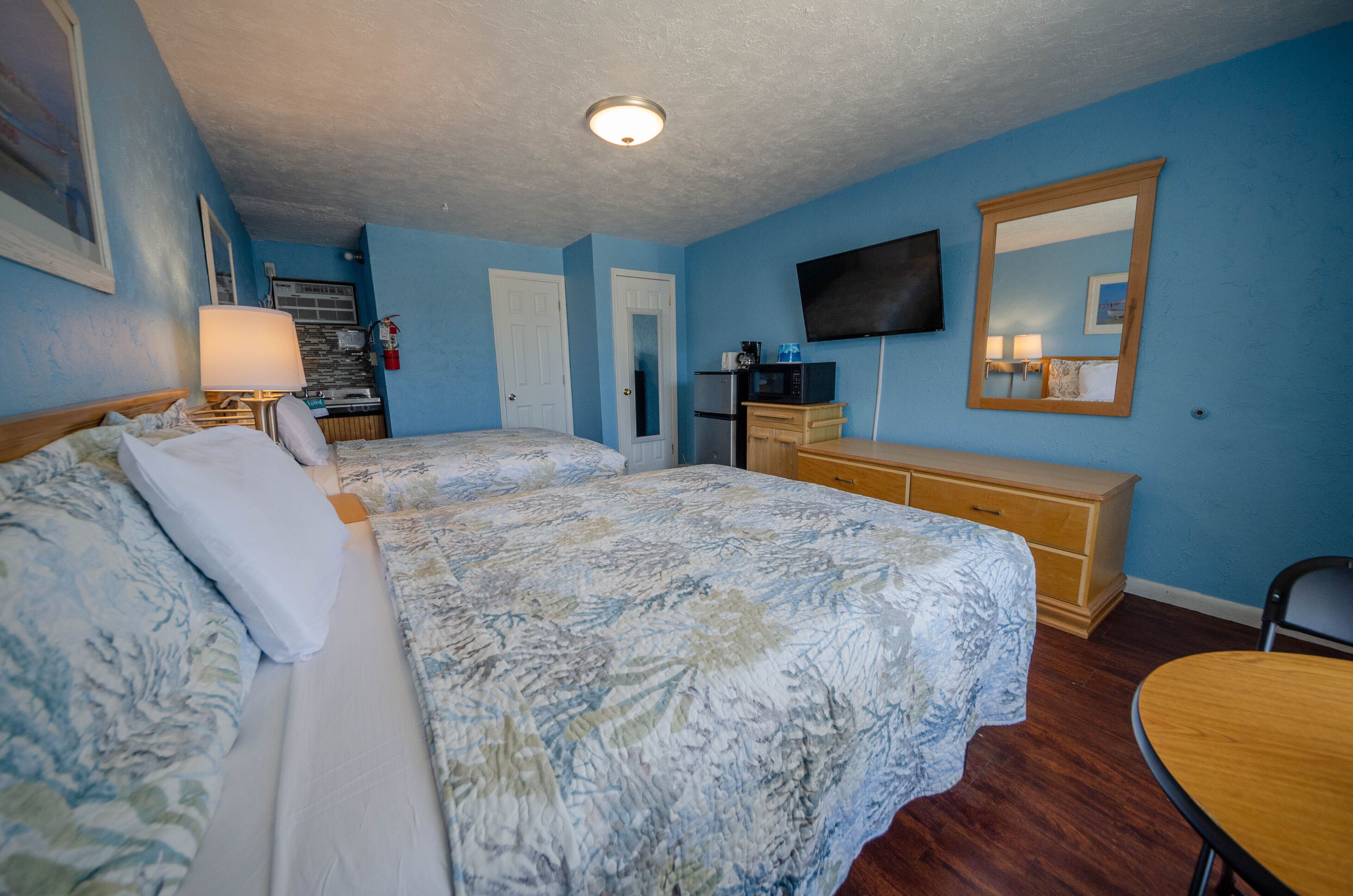 A hotel room with two beds, a desk, a chair, a TV, and a dresser.