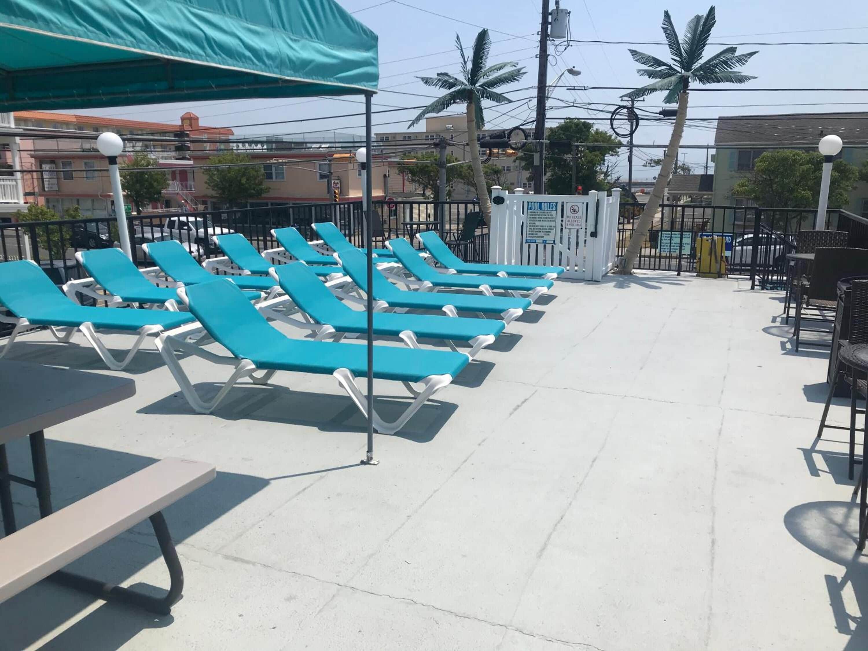 Fila de sillones azules bajo una pérgola, con zona de piscina y un cartel que indica las normas de la piscina.