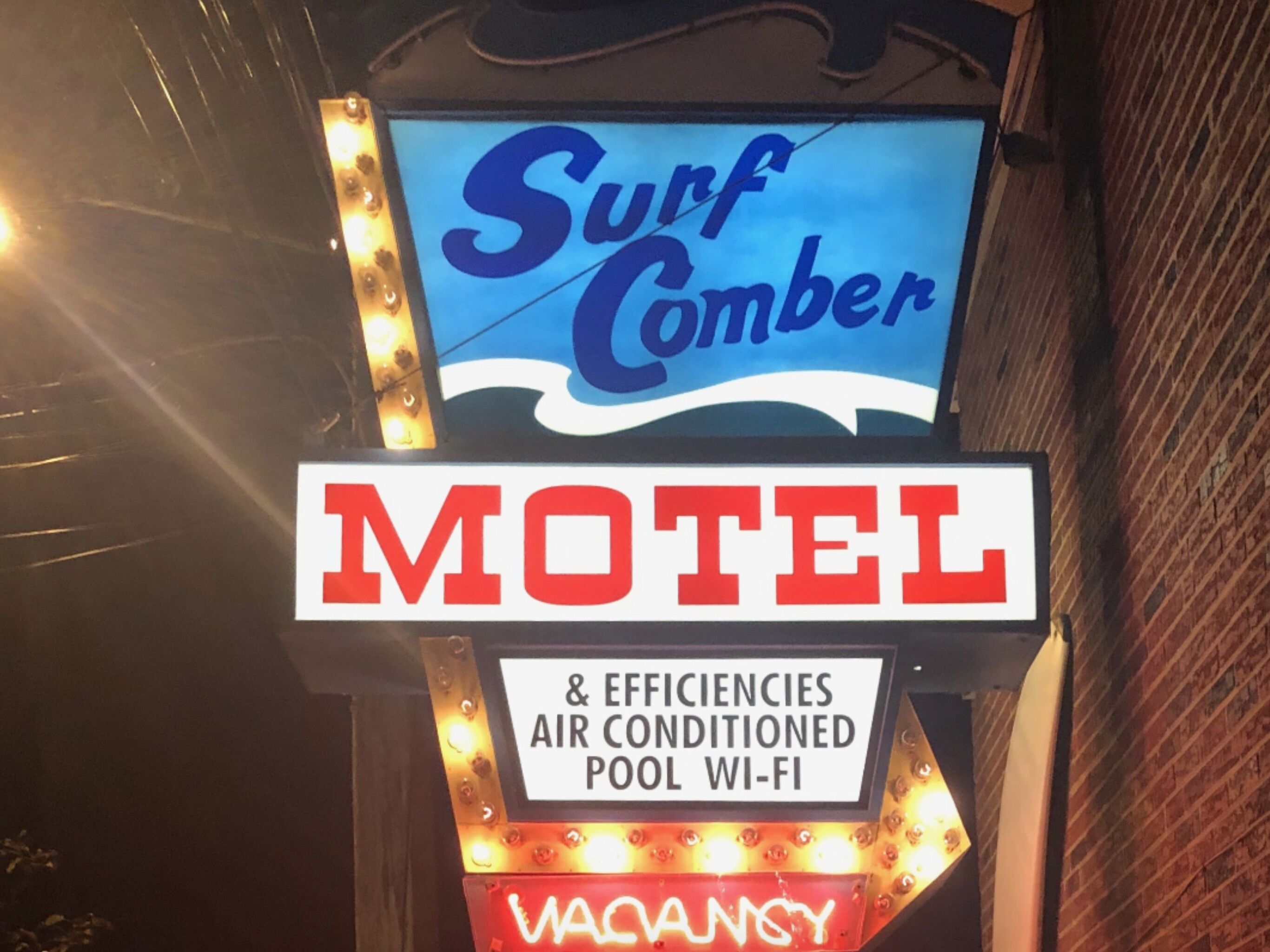 A sign for a Surf Comber Motel with amenities including air conditioning, an air-conditioned pool, and Wi-Fi.