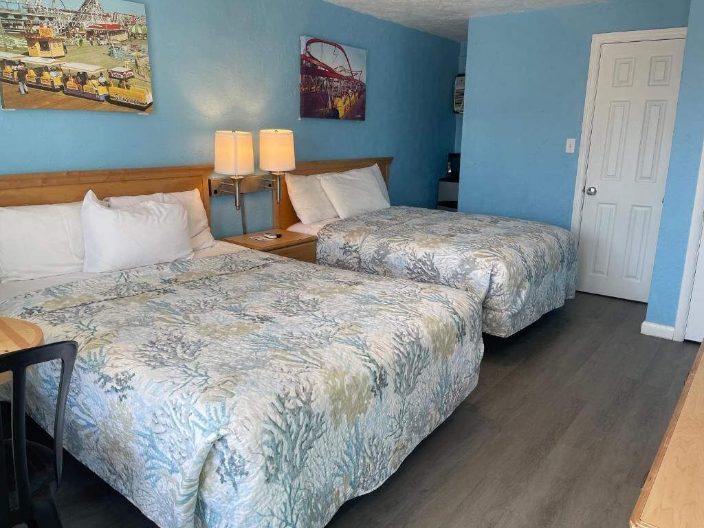 A hotel room with two beds, a desk, a chair, a lamp, and a door.