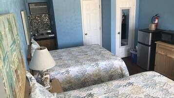 A compact room with a bed, a small kitchenette, and a door leading to another room.