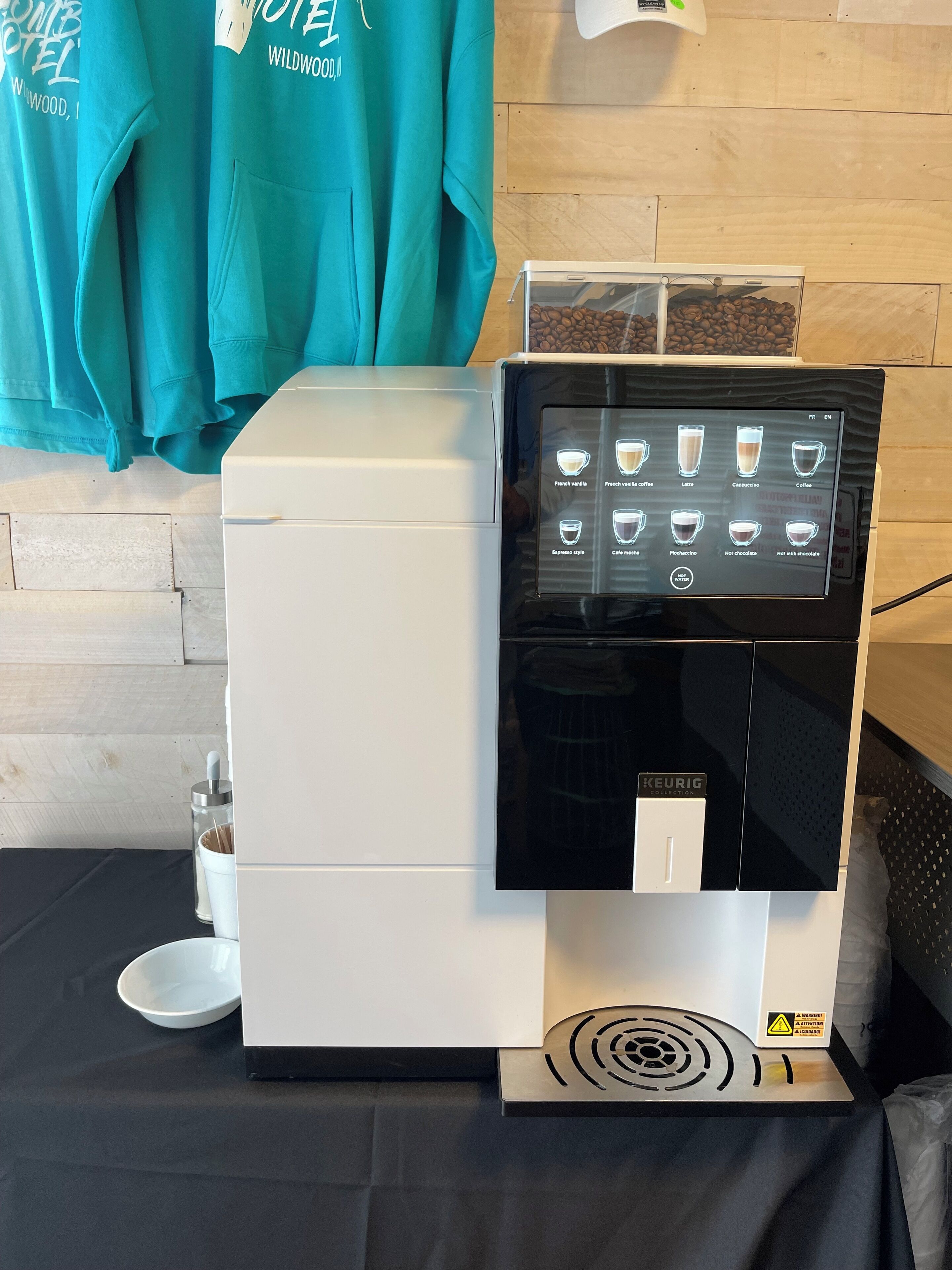 A coffee machine with a digital display menu, a coffee bean container, and a cup of coffee on a table.