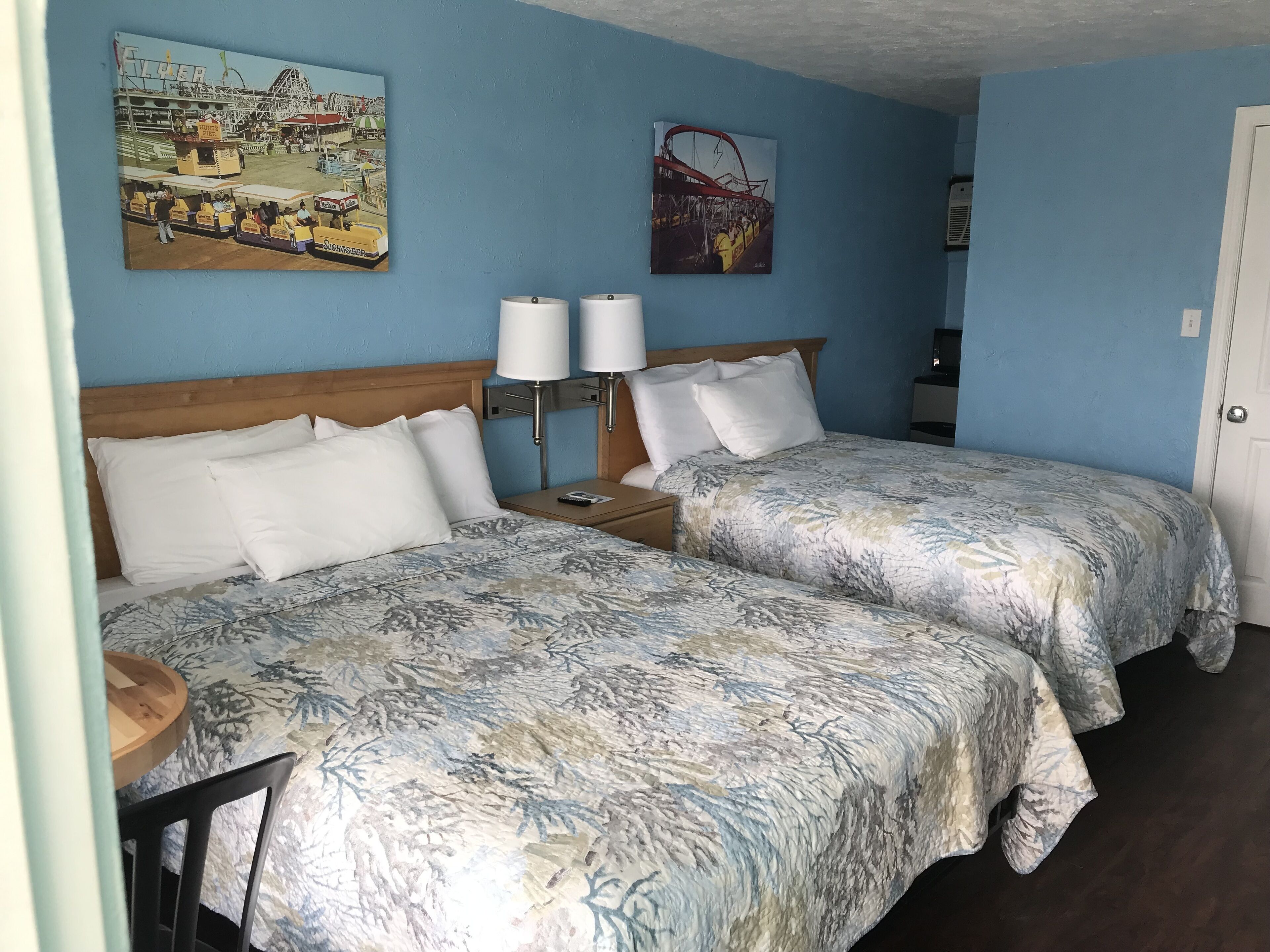 Habitación de hotel con dos camas, cabecera de madera, mesita de noche con lámpara y dos lámparas de pared.
