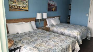 Habitación de hotel con dos camas, cabecera de madera, mesita de noche con lámpara y dos lámparas de pared.