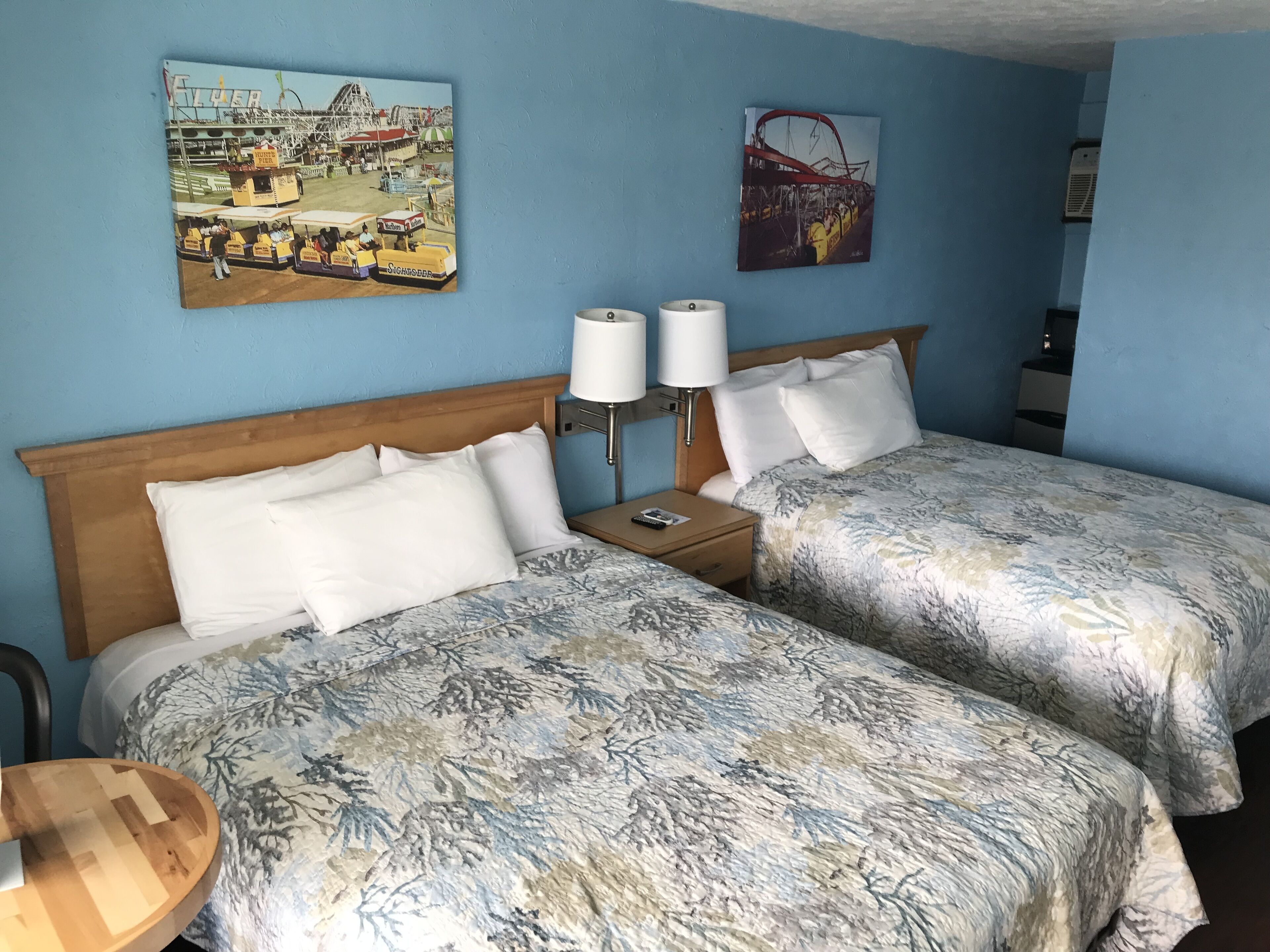 A hotel room with two beds, a nightstand with a lamp, and artwork on the walls.