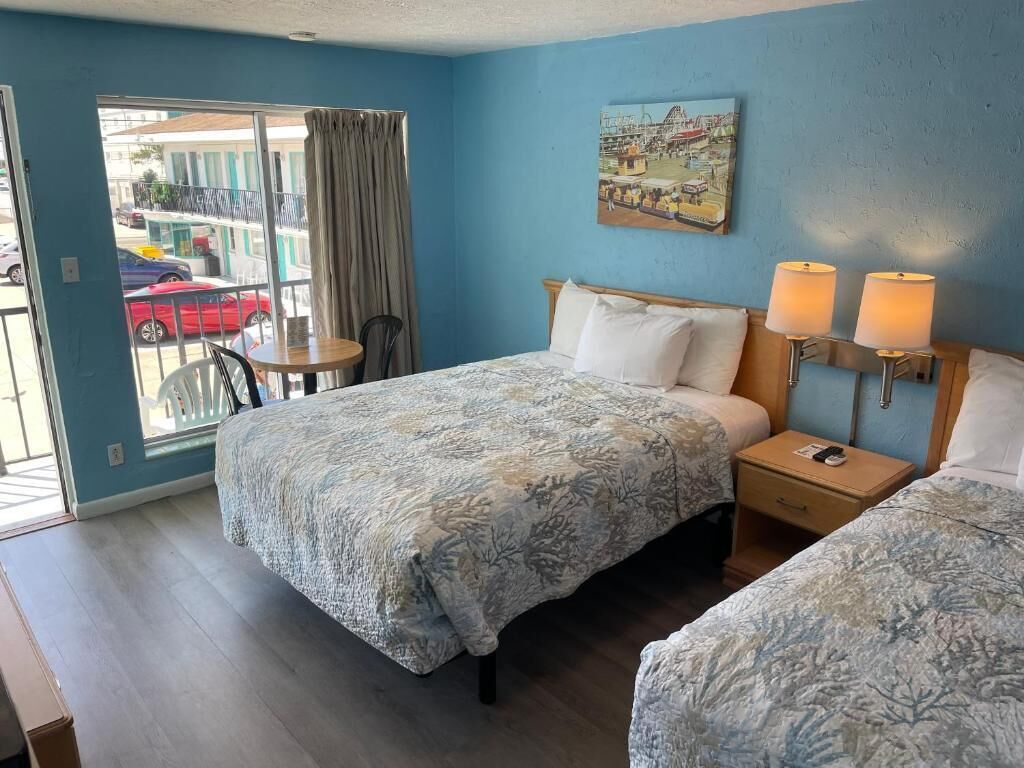 A hotel room with a bed, bedside table, lamp, and a view of the street.