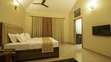 Habitación de hotel con cama, televisión, ventilador de techo y vista al baño.