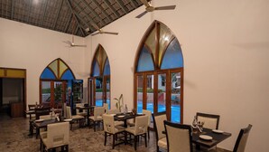 Comedor con varias mesas y sillas, amplias ventanas de arco y ventilador de techo.