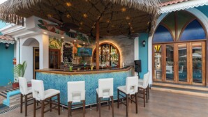 Zona de bar con techo de paja, taburetes blancos y salpicadero de azulejos.