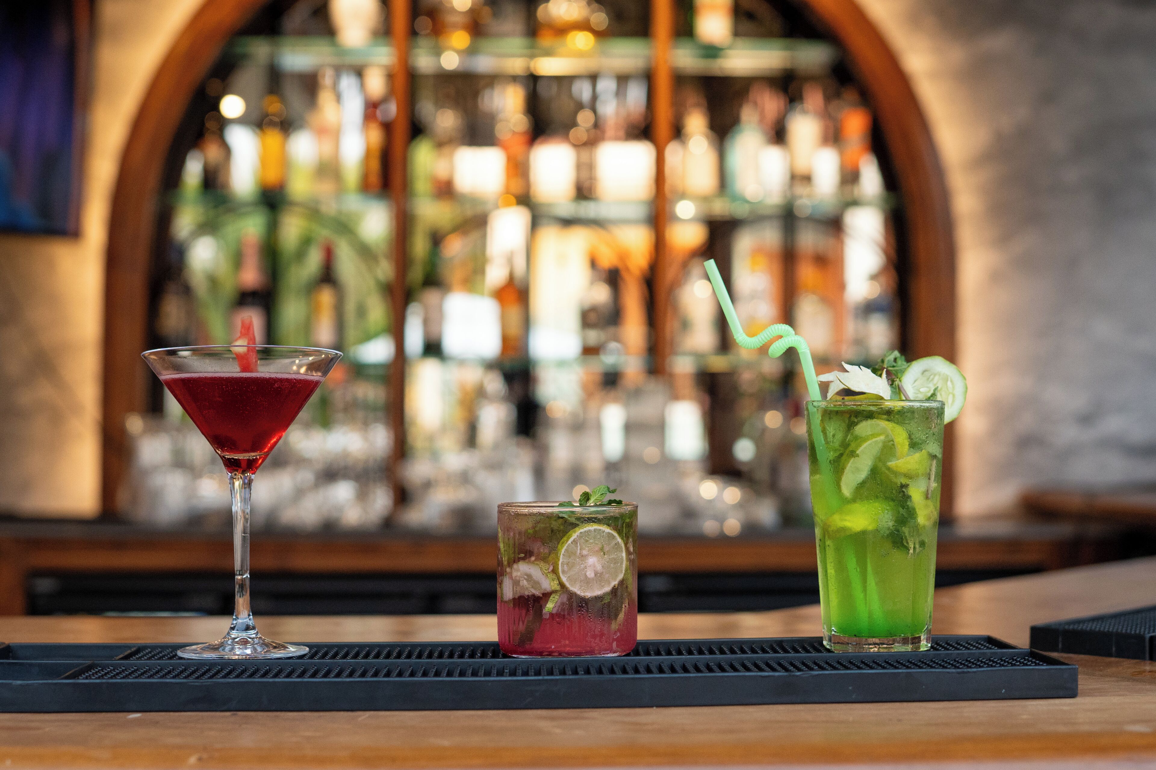 Two cocktails on a bar counter with a blurred background of a bar and shelves.