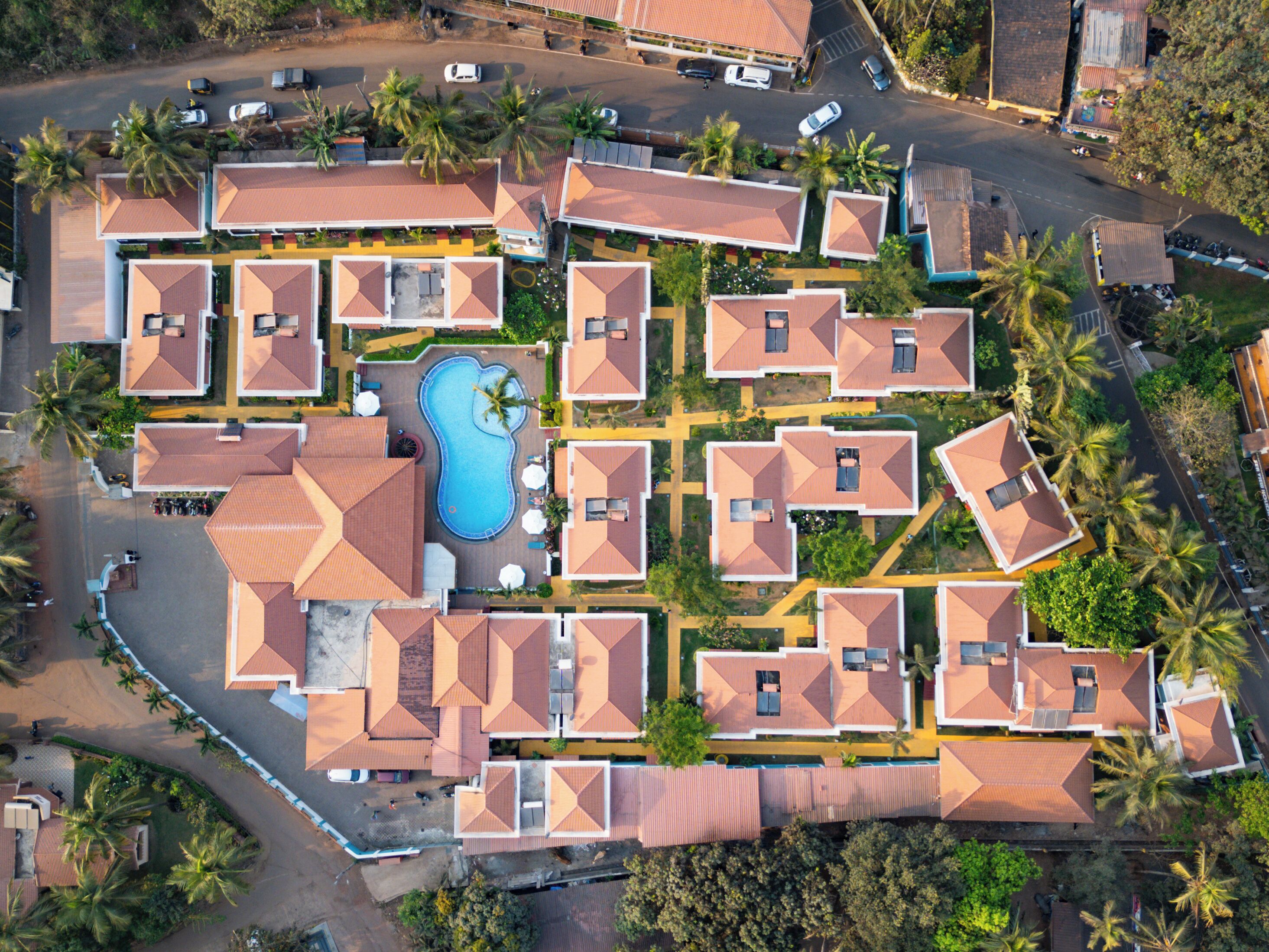Vista aérea de un resort con varias cabañas, una piscina central y palmeras alrededor.