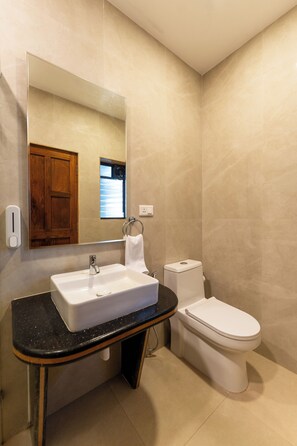 A bathroom with a white sink, a mirror, a toilet, and a wooden cabinet. - The Grand Leoney Resort (Vagator)