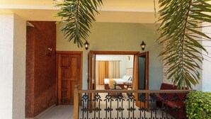 Entrada de hotel con puerta de madera, un balcón con barandilla de hierro forjado y vista a una habitación con cama y cortinas.
