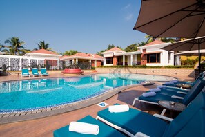 A pool area with lounge chairs and umbrellas, surrounded by buildings with red roofs. - The Grand Leoney Resort (Vagator)