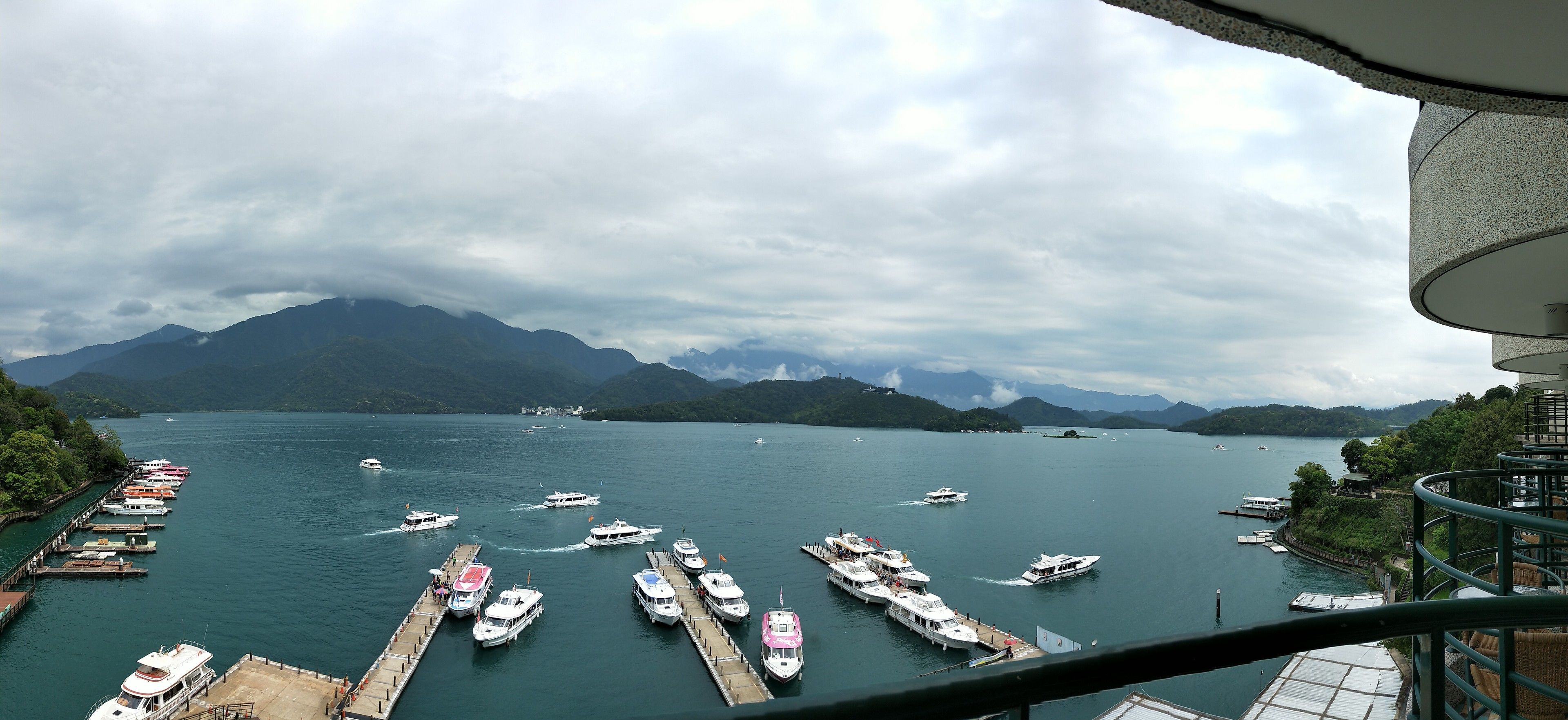 A marina with boats docked, surrounded by mountains and a cloudy sky.