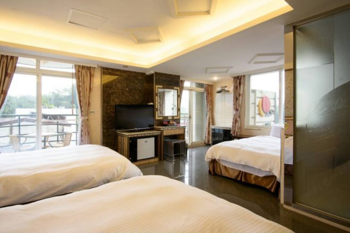 A hotel room with two beds, a TV, a desk, and a balcony view.