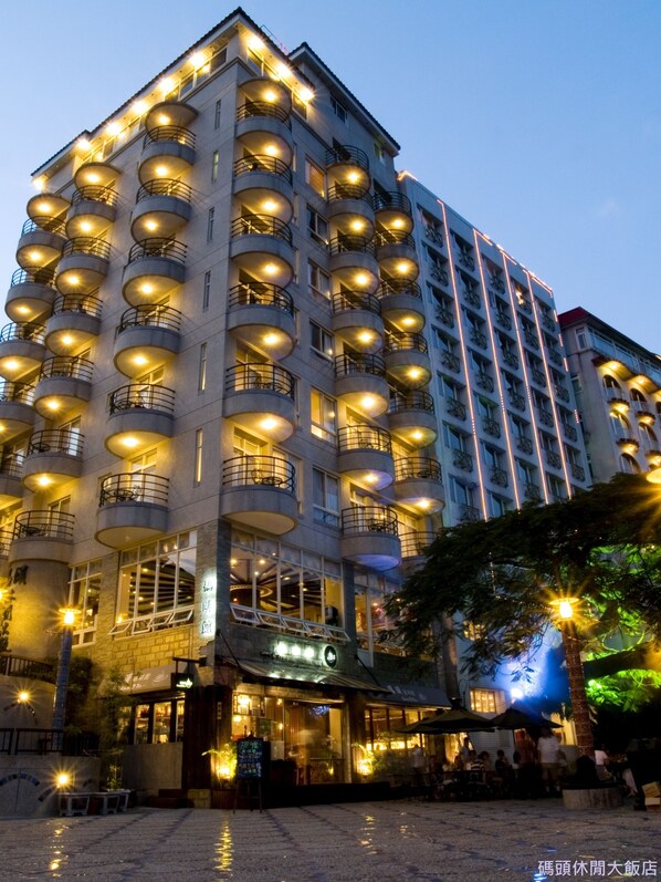 A multi-story hotel with numerous balconies, a ground-level restaurant, and a paved courtyard.