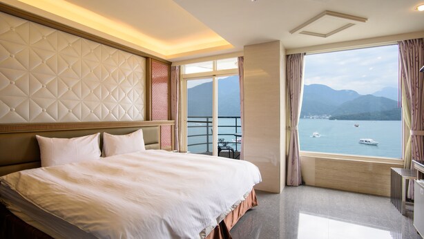 A hotel room with a large bed, a view of the sea, and a balcony with a railing. - 水沙連大飯店-休閒館 (Shui Sha Lian Hotel - Harbor Resort) (Yuchi)