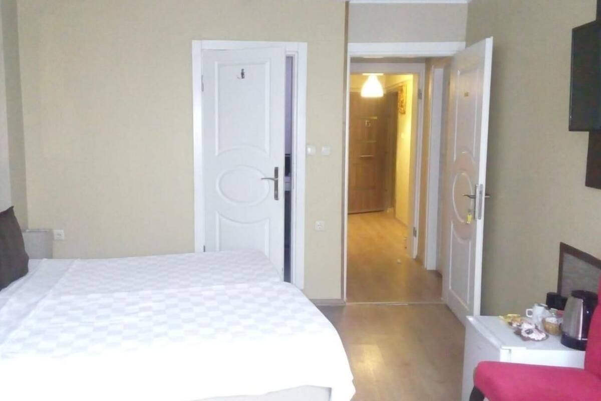 A bedroom with a bed, a nightstand, a red chair, and a hallway leading to another room.