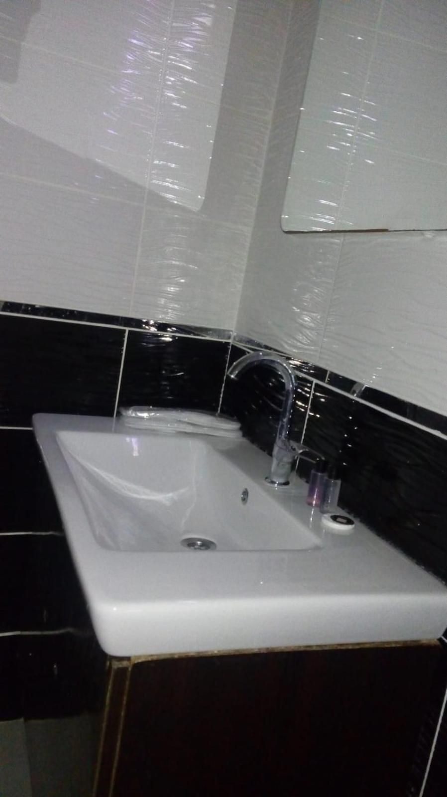 A bathroom with a white sink, black tiled walls, and a mirror above the sink.
