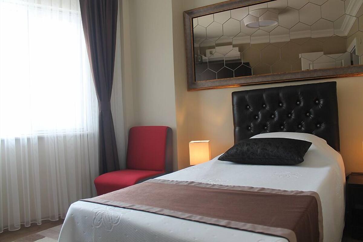 A hotel room with a large bed, a red chair, a bedside lamp, and a mirror on the wall.