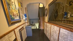 A hallway with a staircase leading to an upper floor, a wall-mounted clock, and a sign instructing to keep social distance. - Lena Central Flats (Bursa)