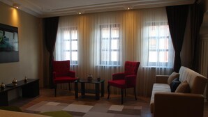 A hotel room with a bed, two red armchairs, a small table, a sofa, and a large window with curtains. - Lena Central Flats (Bursa)