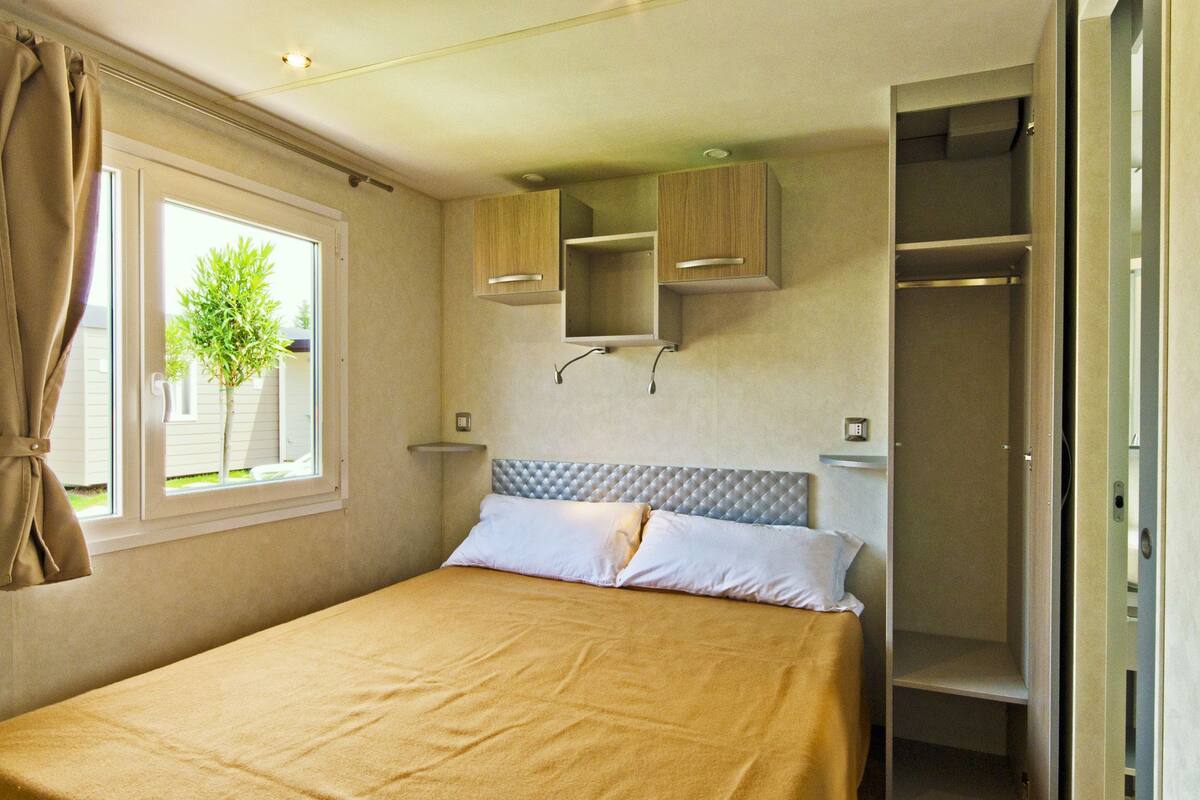 A bedroom with a bed, a window with curtains, a plant outside, and built-in storage cabinets.