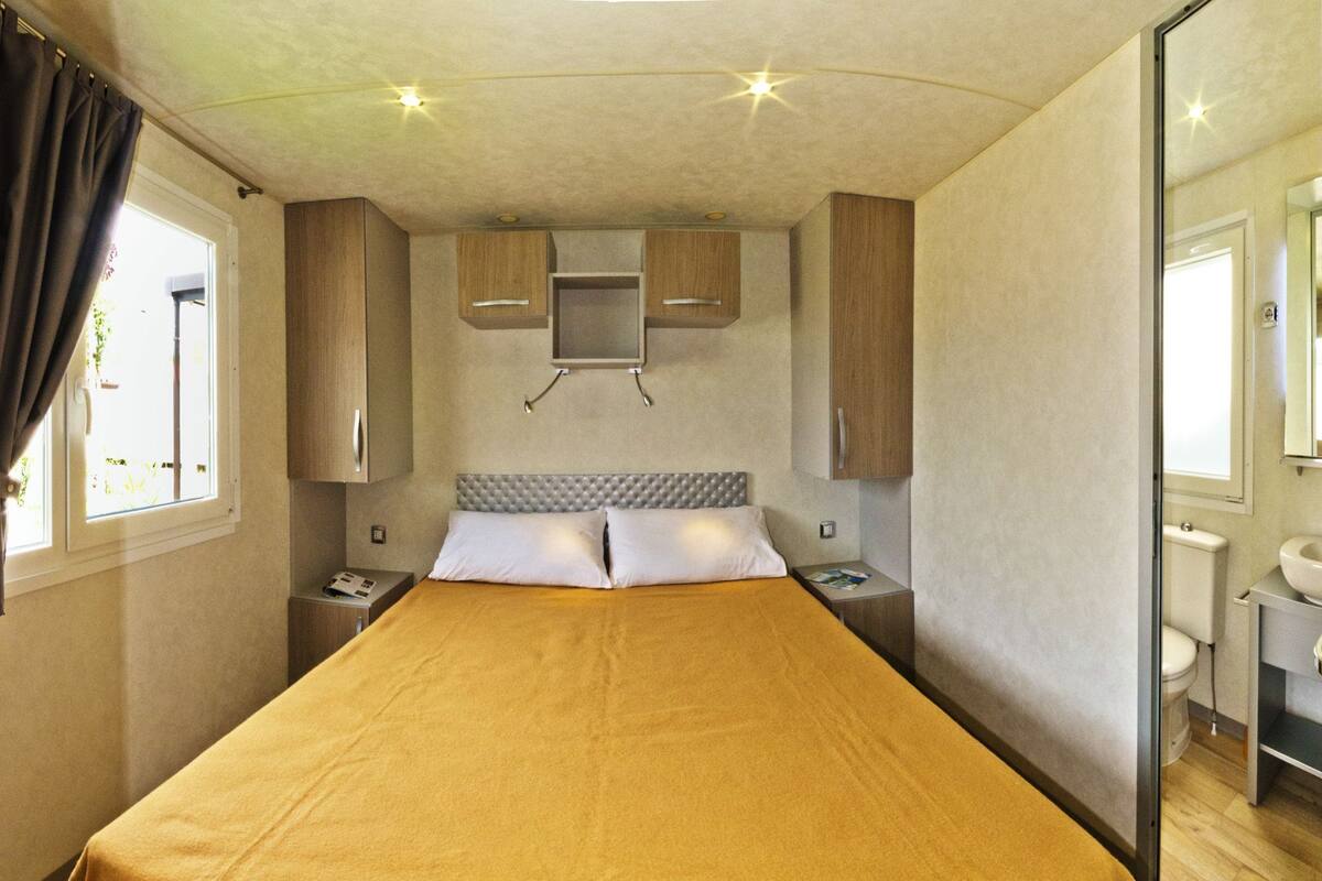 A compact bedroom with a single bed, bedside tables, a small cabinet, and a window with curtains.