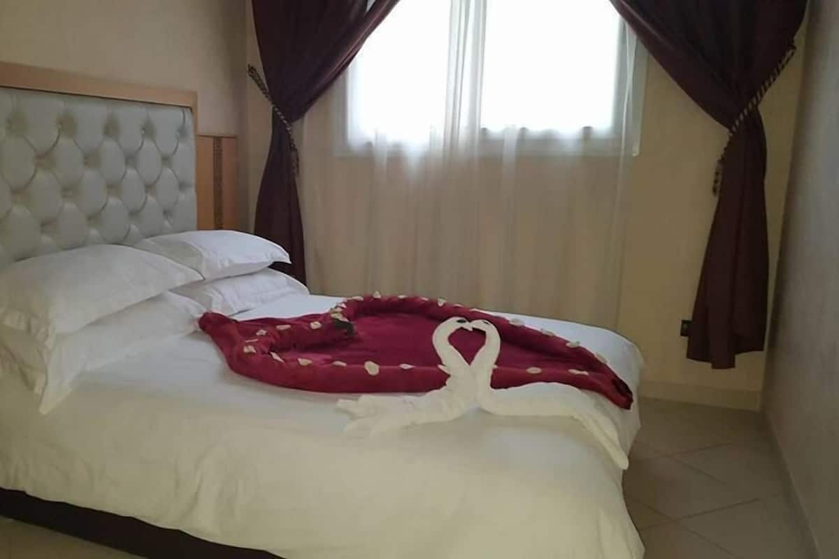 Una cama bien tendida con sábanas blancas y una almohada en forma de corazón rojo.