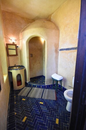 A narrow bathroom with a tiled floor, a sink, a toilet, and a mirror. - Riad Dar El Qdima (Essaouira)