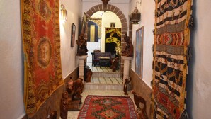 A narrow hallway with ornate rugs, wooden carvings, and a staircase leading to a room. - Riad Dar El Qdima (Essaouira)