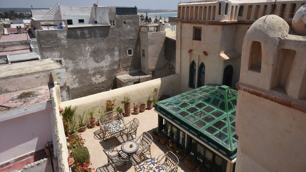 A rooftop terrace with potted plants, outdoor seating, and a view of the sea. - Riad Dar El Qdima (Essaouira)