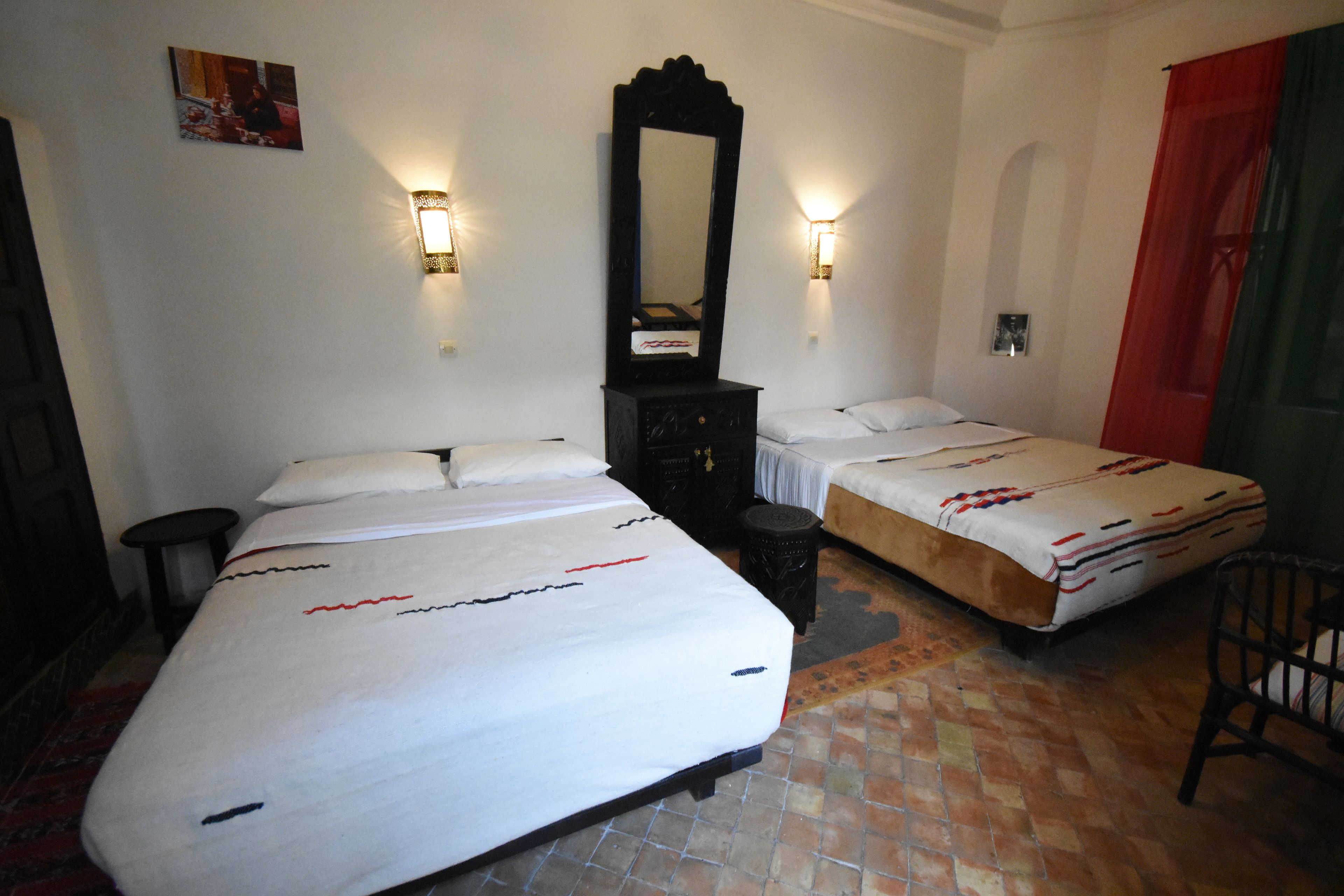 A hotel room with two beds, a large mirror, and wall-mounted lights.