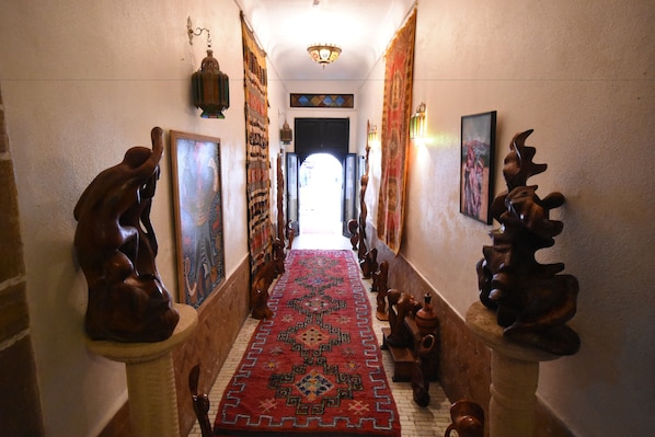 Un couloir orné d’un tapis à motifs, de sculptures en bois et de tableaux encadrés accrochés aux murs.
