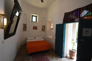Une chambre avec un lit, un miroir, une fenêtre et une porte donnant sur un balcon.