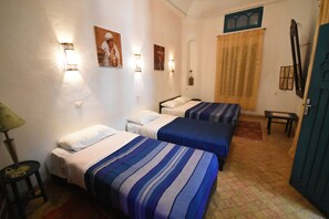 A room with two beds, a small table, a lamp, and wall-mounted lights. - Riad Dar El Qdima (Essaouira)
