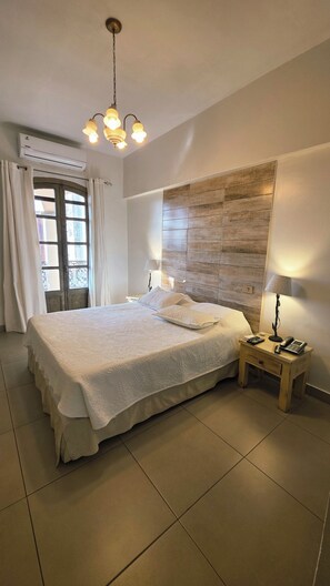 A bedroom with a large bed, a wooden headboard, a nightstand with a lamp, and an air conditioning unit. - Asunción Palace Hotel (Asunción)
